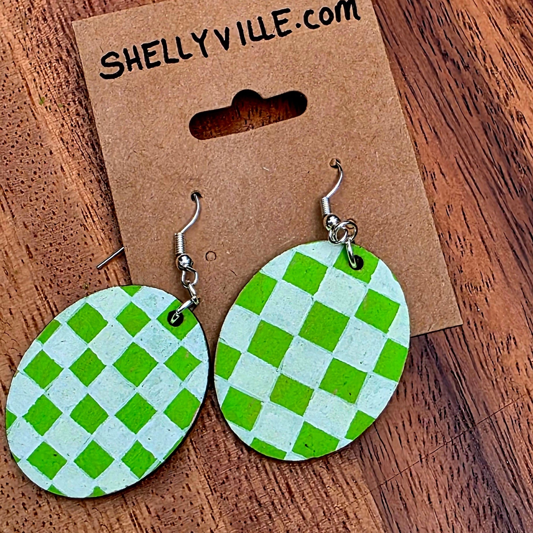 Green checkered earrings on a wooden surface with a 'Shellyville.com' card.