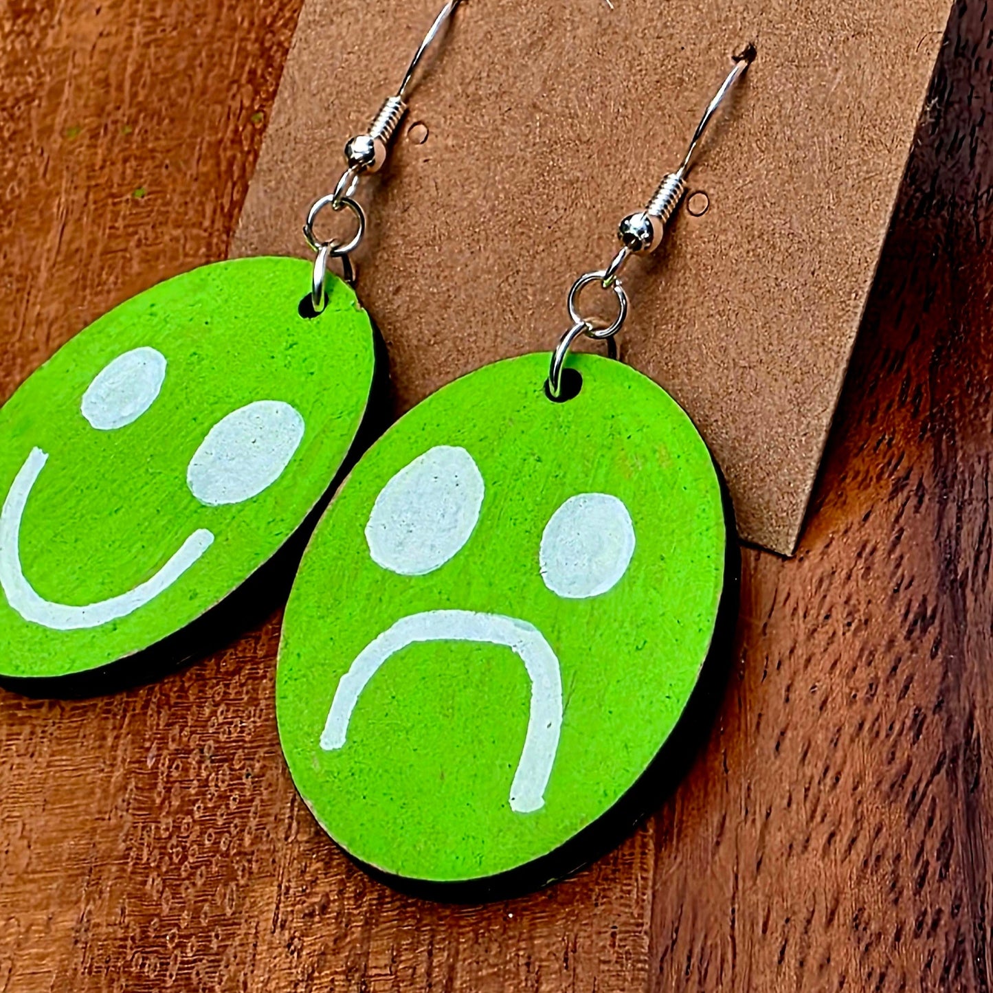 Green smiley face earrings on a brown card with 'Shellyville.com' printed on it, placed on a wooden surface.
